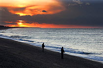Silhouette of two men fishing from beach at  sunset, Weybourne, Norfolk, UK