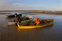 Mussel fisherman with sacks of mussels in his boat, Brancaster, Norfolk, UK, Winter