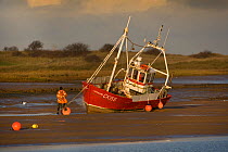 Fishing boat grounded on mud flats at low tide, Brancaster, North Norfolk, UK, winter