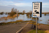 Flood warning sign beside road crossing flooded Old Bedford River, Norfolk, Winter