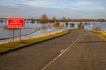 Flood warning sign beside road crossing flooded Old Bedford River, Norfolk, Winter