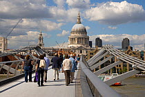 Pedestrians crossing the Millennium Bridge over the River Thames with St Paul's Cathedral in the background, London, UK