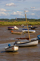 Boats stranded at low tide on the saltmarshes, Morston Quay, Norfolk, UK, with Blakeney Village in the background