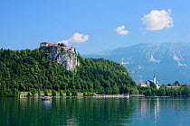 Bled Castle and Succursal Church of St. Andrej overlooking Lake Bled, with tourists on a gondola in the foreground and the Julian Alps in the background, Bled, Slovenia, July 2010.