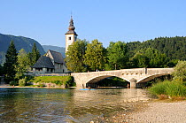 Ribcev Laz church and bridge at the south end of Lake Bohinj, with people walking, fishing, bathing and canoeing in the foreground and forested Julian Alps in the background, Triglav National Park, Sl...