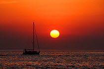 Sailing yacht silhouetted at sea off Zadar as the sun sets, with Pasman island in the far background, Croatia, July.