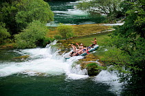Tourists approaching a small travertine dam waterfall on the Mreznica river in an inflatable white water raft, Zvecaj, Karlovacka, Croatia, July.