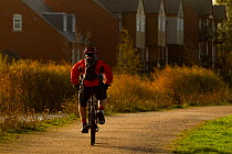 Man riding bike down path by a river with houses in background, The National Forest, Central England, UK, November 2010