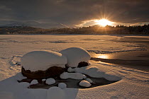 Loch Morlich frozen over with low winter sun shining through clouds, Cairngorms NP, Highlands, Scotland, UK, December 2010