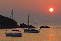 Sunset over a bay with two sailing boats at anchor. East coast of Corsica, Mediterranean Sea, France, Europe, September 2005.