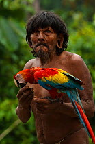 Huaorani man with his pet Scarlet Macaw (Ara macao). Gabaro Community, Yasuni National Park, Ecuador, June 2007. Model release #GA03.