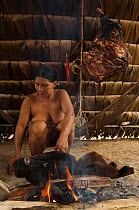 Huaorani Indian woman cooking a woolly monkey. Gabaro Community, Yasuni National Park, Ecuador, June 2007. Model release #GA15.