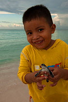 A child holding a newly hatched turtle. Marine Turtle Sanctuary of Xcacel and Xcacelito, Quintana Roo, Yucatan Peninsula, Mexico. Model release #YP1.