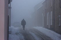 Pedestrian in freezing fog and heavy snow walking along town street, Denbighshire, North Wales, UK, December 2010