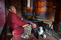 Buddhist pilgrim sitting by a prayer wheel in Galdan Namge Lhatse monastery. Tawang, Arunachal Pradesh, India, February 2011.
