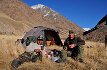Photographer Eric Dragesco and guide resting outside their tent, on expedition to find Tien Shan Argali (Ovis ammon karelini). Naryn National Park, Kyrgyzstan, Central Asia, November.