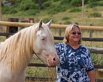 Photographer, Carol Walker, leading young male cremello Wild horse / mustang Claro that had been rounded up from a McCullough Peak herd and put up for adoption, August 2010, model released