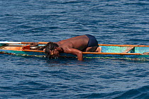 Hook and line fishermen in his dugout canoe wearing self-made goggles to target the fish that he aims to catch, Indonesia, November 2009.