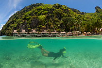Snorkeler swimming underwater, split level, with Miniloc Island Resort in the background, El Nido, Palawan, Philippines, May 2009. Model released