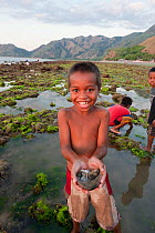 Child holding out bowl of produce from gleaning on coast at low tide for marine invertebrates and small fish and algae, East Timor, August 2010.