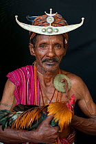 Portrait of East Timorese man in traditional clothing adn head dress, with cockerel, Maubara, East Timor, August 2010.