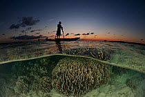 Split level image of Papuan fisherman standing on his dugout canoe over shallow corals, New Ireland, Papua New Guinea, June 2010