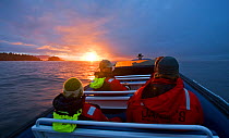 People in a small boat with the sun setting on the horizon. Pacific Rim National Park, Vancouver Island, Canada, September 2010, model released