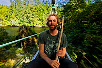 A man sitting in the cable car of a chair bridge as it crosses a river. The West Coast Trail, Pacific Rim National Park, Vancouver Island, Canada, September 2010. Model released
