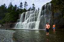 Two men at the foot of a large waterfall. The West Coast Trail, Pacific Rim National Park, Vancouver Island, Canada, September 2010.