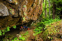 Hikers resting under an overhanging cliff on the West Coast Trail. Pacific Rim National Park, Vancouver Island, Canada, September 2010.