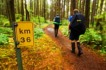 Hikers passing a sign informing them that they either have 36km to go, or have come 36km. The West Coast Trail, Pacific Rim National Park, Vancouver Island, Canada, September. Models released.