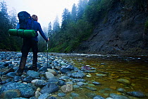 A hiker by a river bedded with rocks worn smooth by the waters. The West Coast Trail, Pacific Rim National Park, Vancouver Island, Canada, September 2010. Model released.