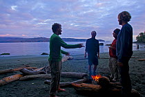 Hikers talking as they warm themselves by a campfire on a beach. The West Coast Trail, Pacific Rim National Park, Vancouver Island, Canada, September 2010. Models released.