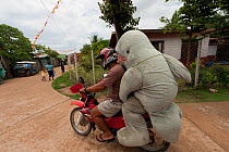 Mascot 'Waddy', part of a conservation project for the Irrawaddy dolphin (Orcaella brevirostris), getting a lift home on a motorcycle. North Palawan, Philippines, May 2009.