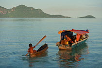 Child in canoe beside traditional fishing boat, Semporna, Sabah, Borneo, Malaysia, June 2009.