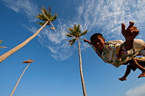 Bajau boys playing on a rope swing hung high up in two tall coconut trees. Sibuan Island, Malaysia, June 2009.