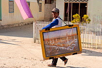 Picture vendor walking along a street to sell his wall photographs. Here he brings Mecca to people's doorstep. Wanci, Wakatobi, Sulawesi, Indonesia, October 2009.