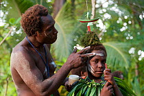 Man applying lime paste to the face of a boy for a sing-sing performance, known as laklakau in the Tigak language, by Enuk villagers.  Kavieng, Papua New Guinea, June 2010.