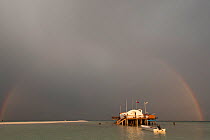 Tubbataha Reef ranger station in a storm with a full arch rainbow against the dark clouds. Tubbataha Reef National Marine Park, Palawan, Philippines, April 2009.