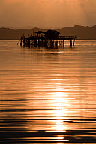 Fish farm houses on stilts in sea at sunset. Under the house are live reef fish cages serving as a grow-out farm for the live reef fish trade. Northern Palawan, Philippines, April 2009.