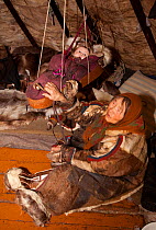 Nyaka, an elderly Nenets woman, rocks her grandaughter in a cradle inside their reindeer skin tent. Tambey tundra, Yamal Peninsula, Western Siberia, Russia. March 2011