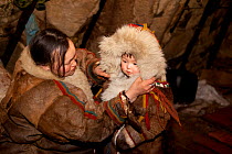 Emma Vanuito, a Nenets woman, dresses her daughter, Nenya, in traditional warm fur clothing so she can go outside and play in the cold. Tambey. Yamal Peninsula, Western Siberia, Russia. March 2011