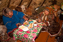 Vadim Vengy, a Nenets reindeer herder, having a meal with 76 year old Nyaka inside her reindeer skin tent. Tambey, Yamal Peninsula, Western Siberia, Russia, March 2011