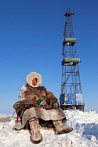 Jakov Vanuito, a Nenets reindeer herder, sits infront of a gas drilling derrick near Tambey in the South Tambey gas field. Yamal Peninsula, Western Siberia, Russia, March 2011