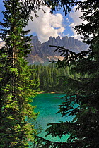 The lake Lago di Carezza / Karersee surrounded by mountain peaks and pine forest in the Dolomites, Italy, July 2010.