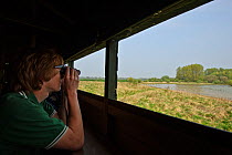 Young man viewing Rutland Water with binoculars from bird hide, Rutland, UK, April 2011