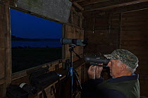 Volunteer Warden, Ray Sykes, using night vision optics to observe the Manton Bay osprey pair at night, Rutland Water, Rutland, UK, April 2011. During the incubation period the Osprey nest is observed...