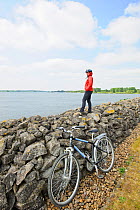 Young woman cyclist standing on stone wall viewing Rutland Water, Rutland, UK, April 2011, Model released