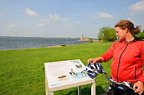 Young woman cycling round Rutland Water, stopping to read information board, Rutland, UK, April 2011, Model released.