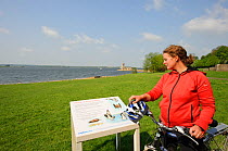 Young woman cycling round Rutland Water, stopping to read information board, Rutland, UK, April 2011, Model released.